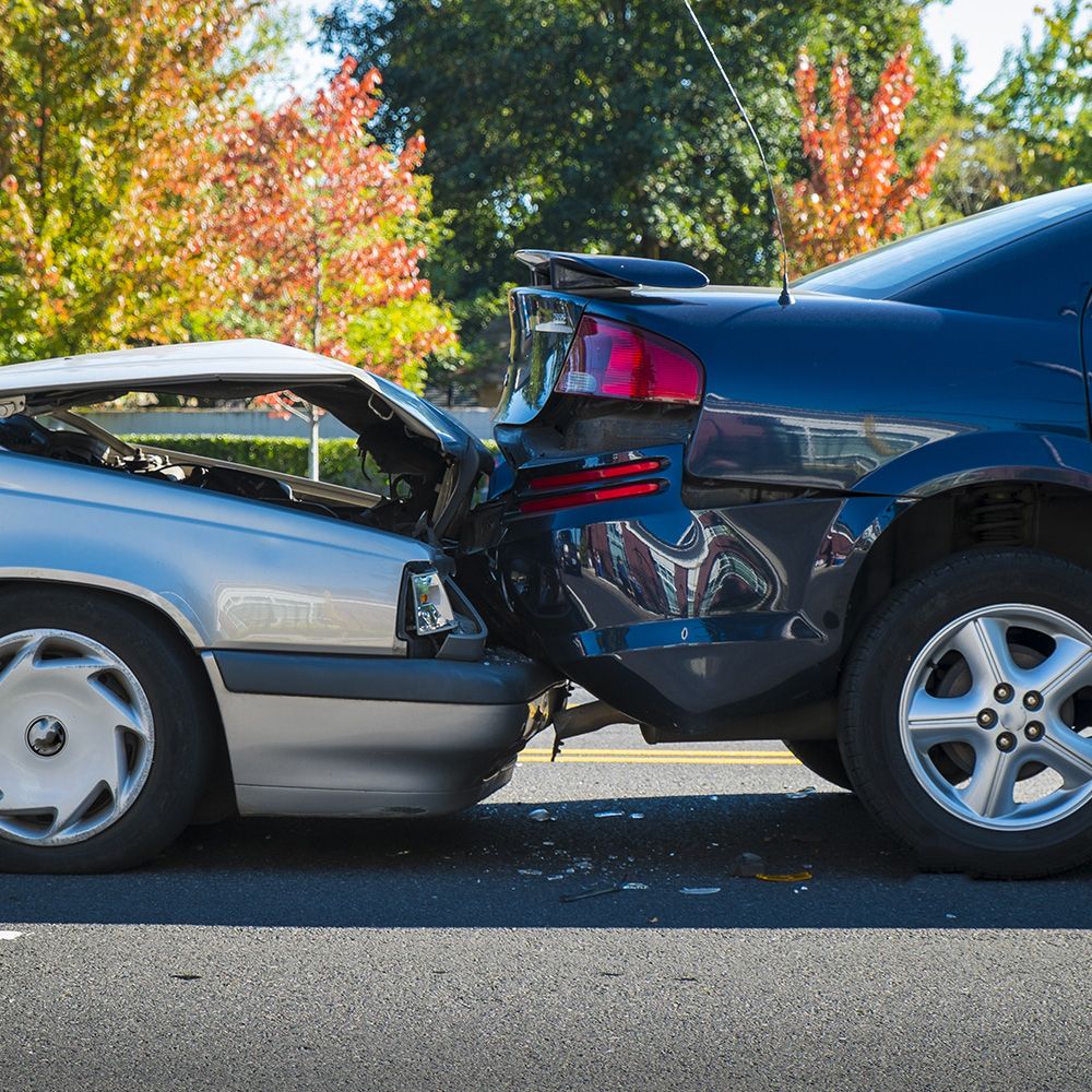 Zwei Autos bei einem leichten Zusammenstoß: eine silberne Limousine mit zerknitterter Motorhaube und ein schwarzer Geländewagen mit Heckschaden vor einer Kulisse aus Bäumen.